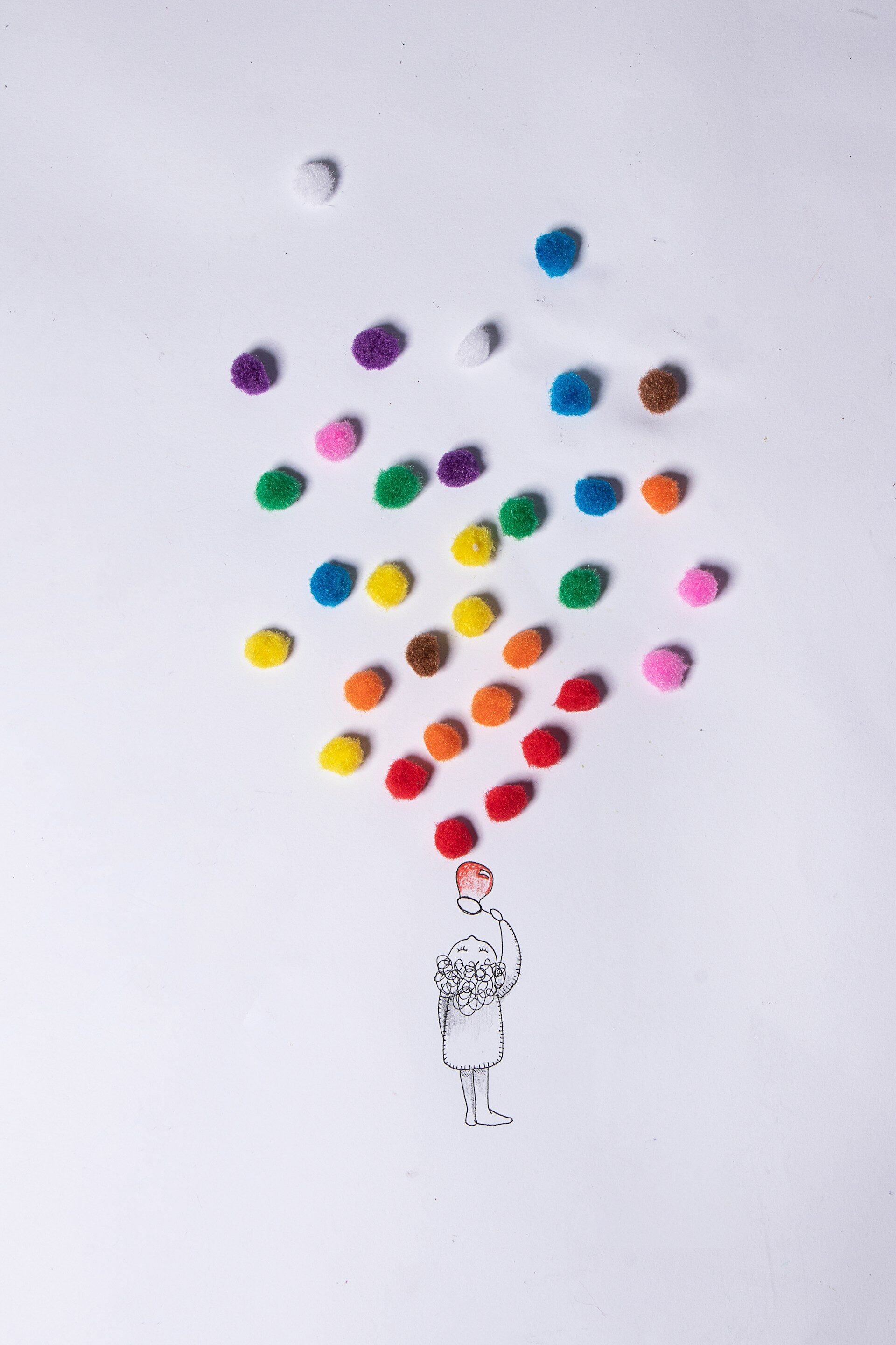 Eine mit Bleistift gezeichnete Figur bläst bunte Seifenblasen. Die Blasen sind auf dem Papier liegende bunte Stoffkugeln. 