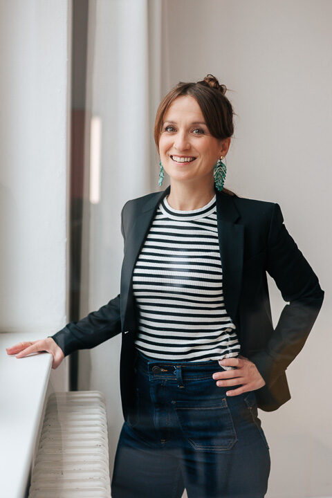 Nicole Forrai steht in einem Raum, in dem sie Führungskräfte Coachings durchführt und lächelt freundlich in die Kamera.