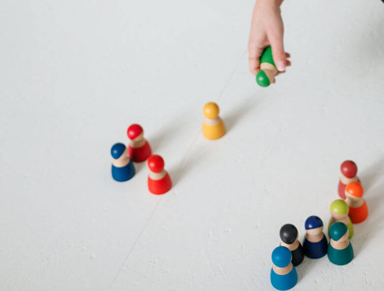 Nicole Forrai hält eine gründe Spielfigur in der Hand. Auf dem Boden stehen weitere bunte Spielfiguren, die im systemischen Coaching die Zusammensetzung und Dynamiken im Team visualisieren.