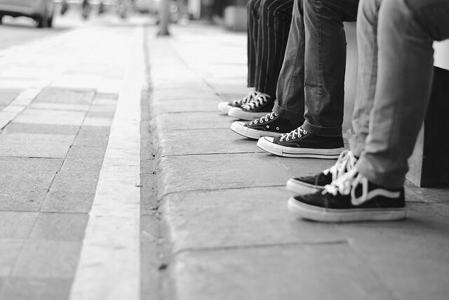 Drei Leute sitzen an einer Bushaltestelle. Zu sehne sind nur ihre Beine und Füße. Das Bild steht für die Teamphasen, in denen sich Teams befinden können. 